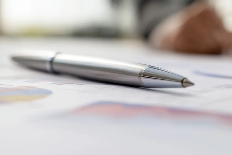 Silver pen resting on financial report with charts and graphs on desk