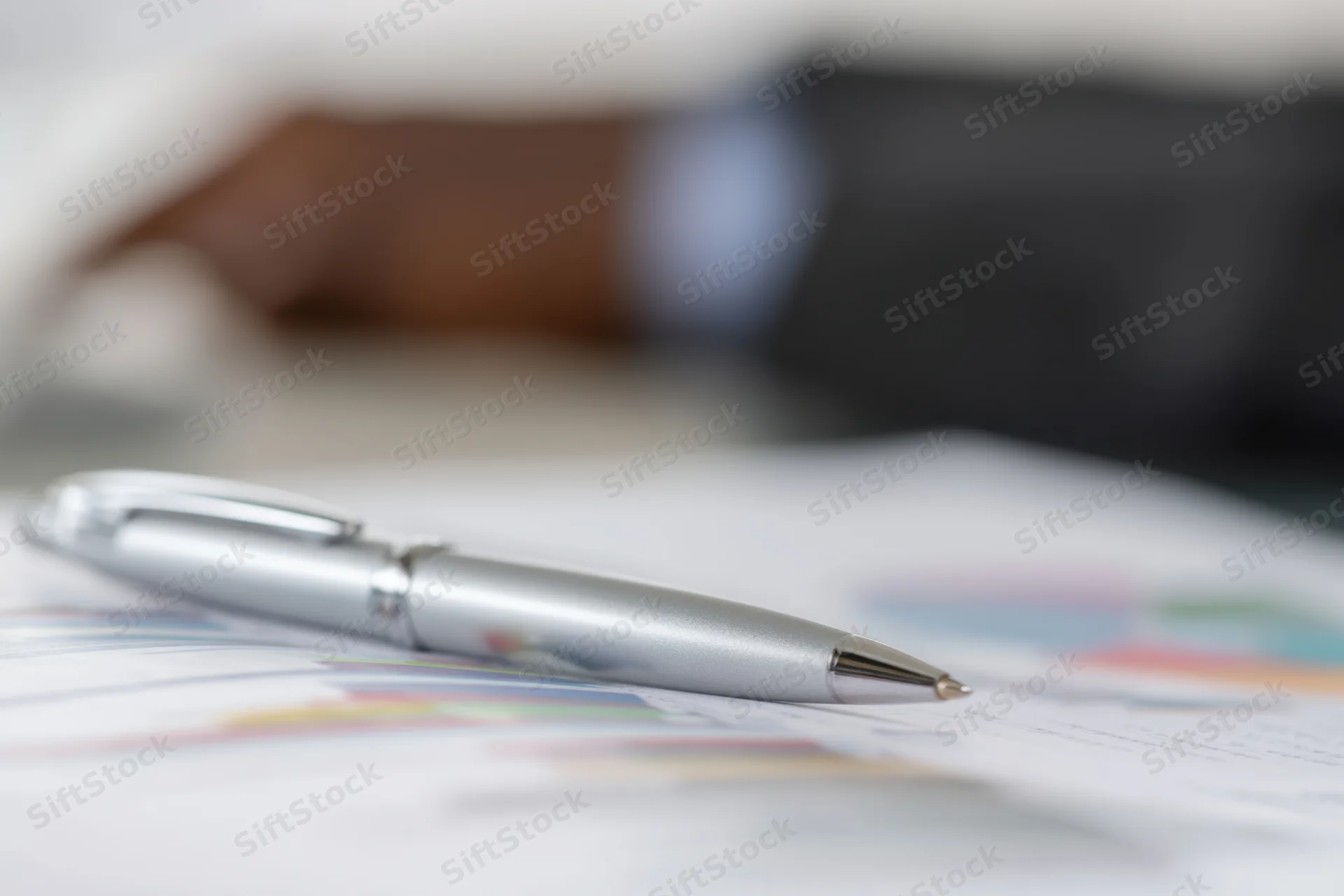 Silver pen resting on financial report with charts and graphs on desk