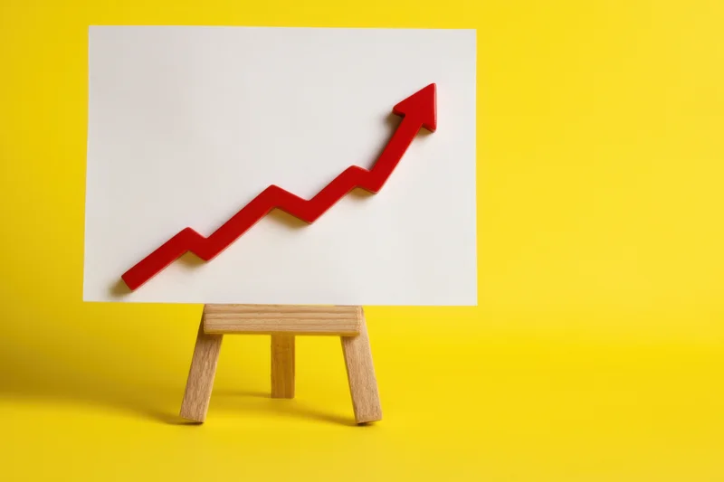 Red upward arrow on white board displayed on wooden easel against yellow background