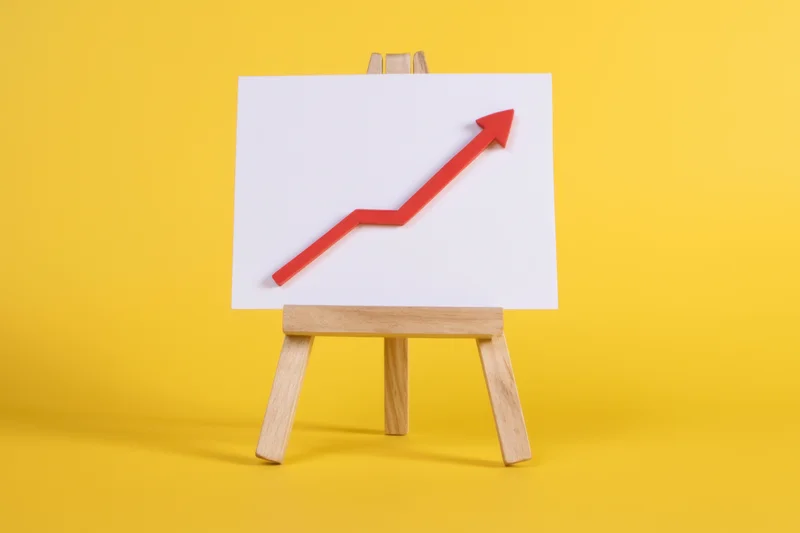 Wooden easel holding white board with red upward arrow on yellow background