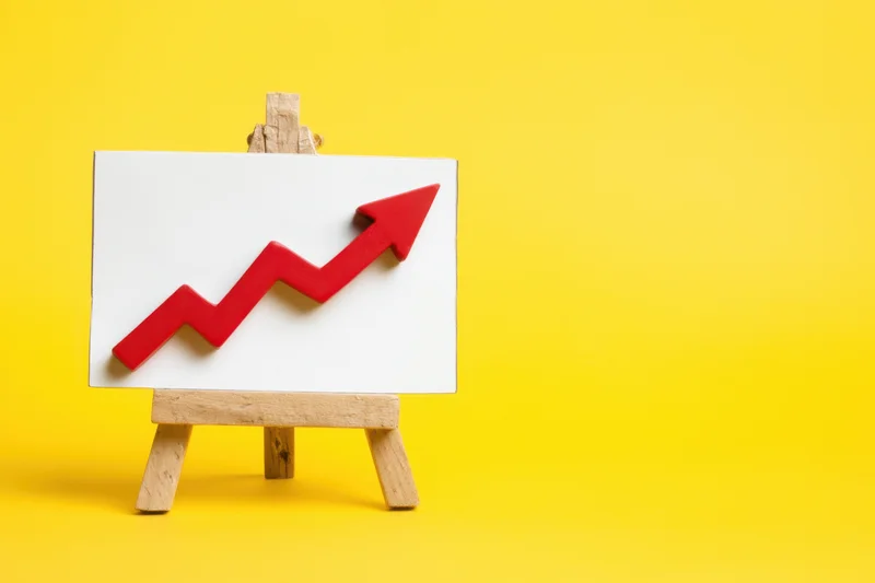 Red upward arrow on white board displayed on wooden easel against yellow background