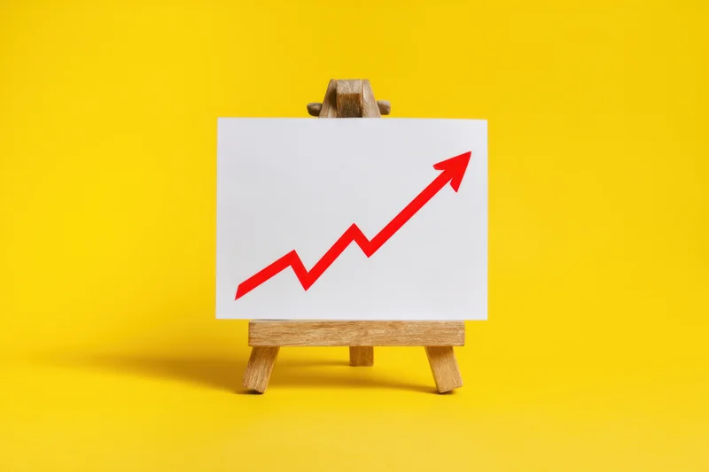 Small wooden easel displaying white board with red upward arrow on yellow background