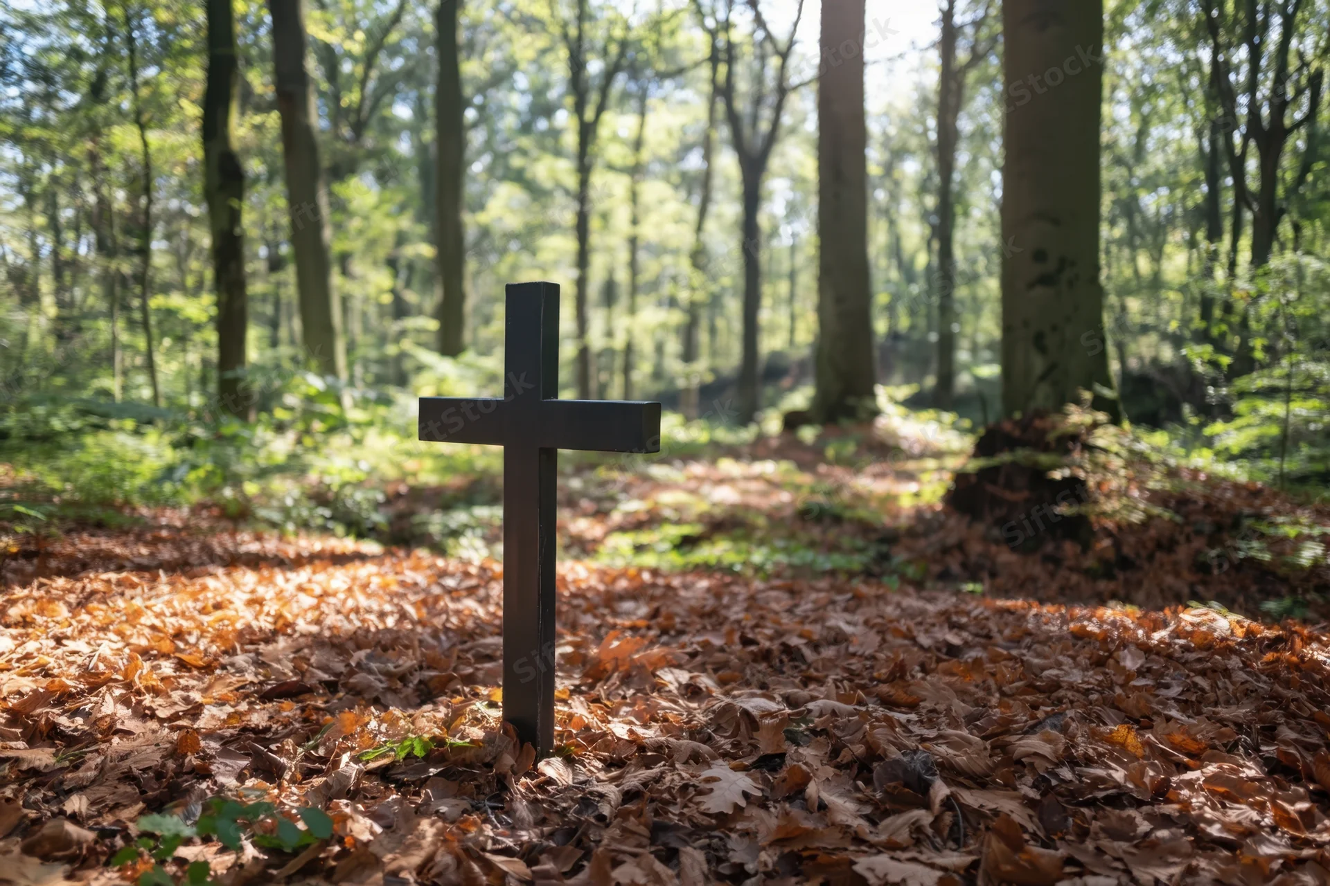 Black cross standing in a forest floor covered with autumn leaves