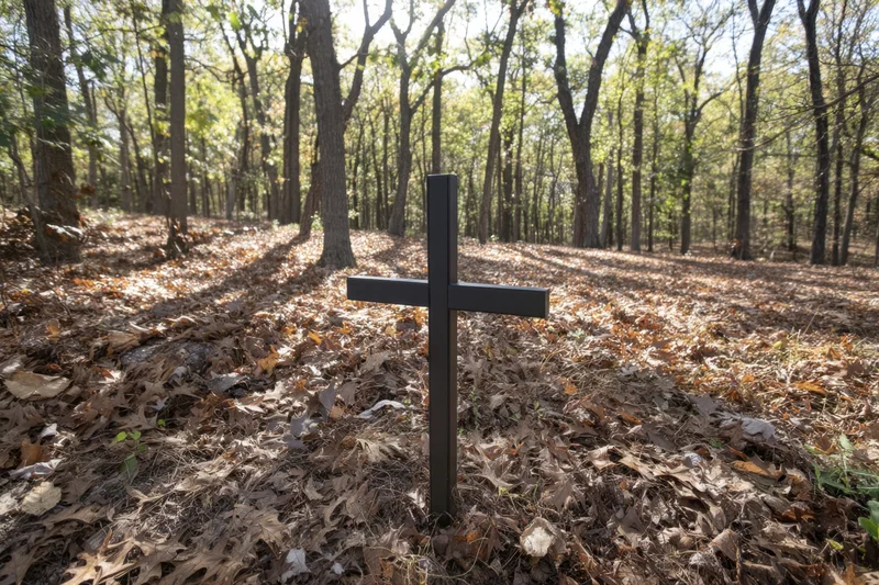 Black cross standing in a forest clearing covered with autumn leaves