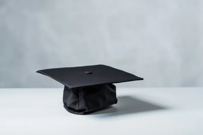 Black graduation cap resting on a white surface against a gray background