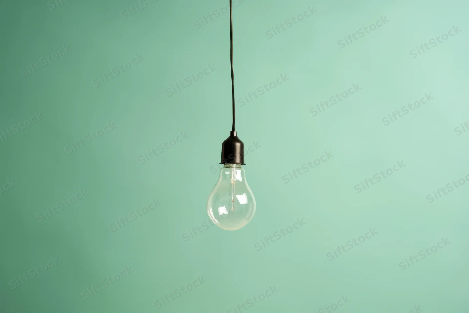 A single incandescent lightbulb hanging from a black cord against a plain green background