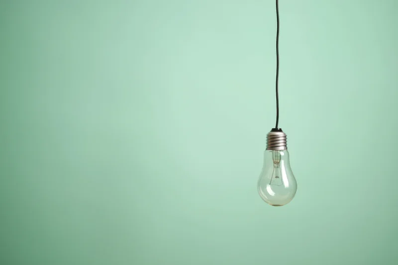 A single lightbulb hanging from a thin black cord against a plain green background
