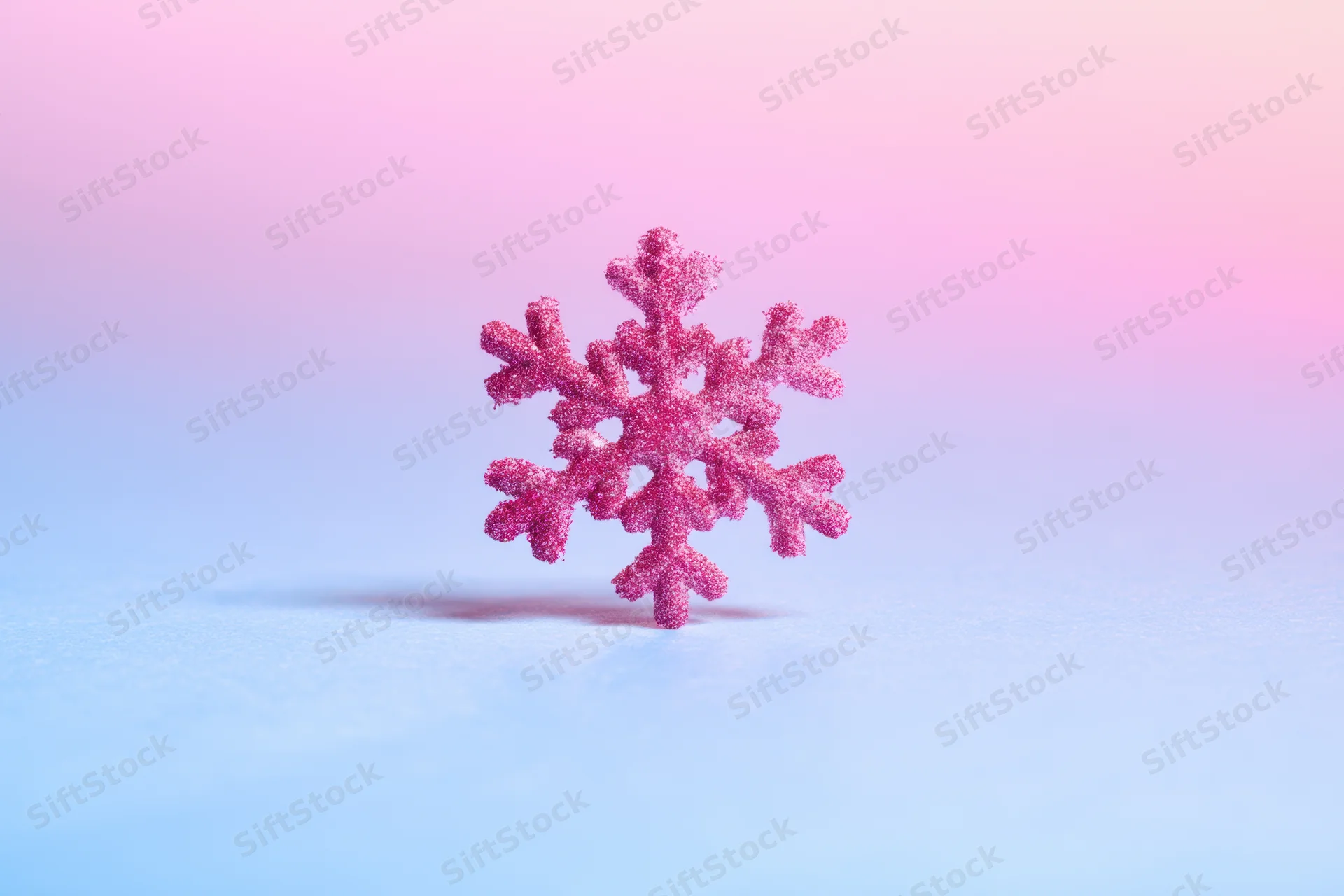A sparkling pink glitter snowflake decoration on a soft blue and pink gradient background