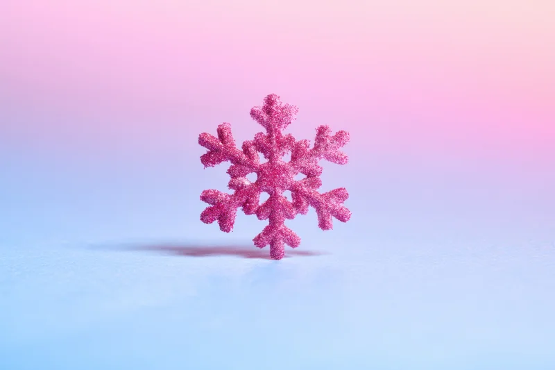 A sparkling pink glitter snowflake decoration on a soft blue and pink gradient background
