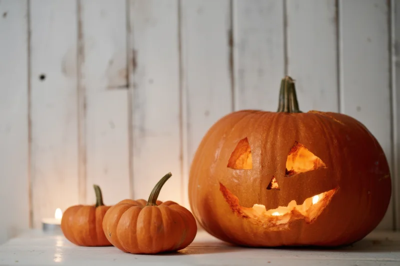 Carved pumpkin with glowing face and small pumpkins on wooden table