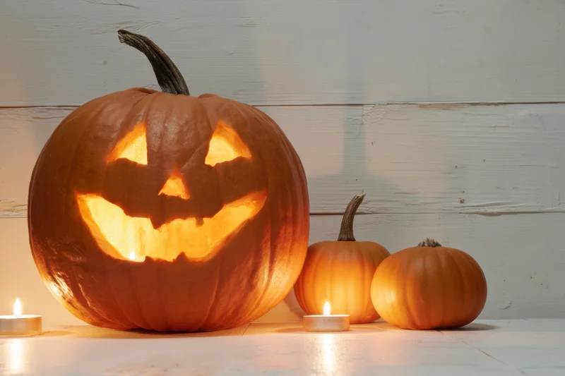 Carved pumpkin with glowing face and candles on white surface beside smaller pumpkins