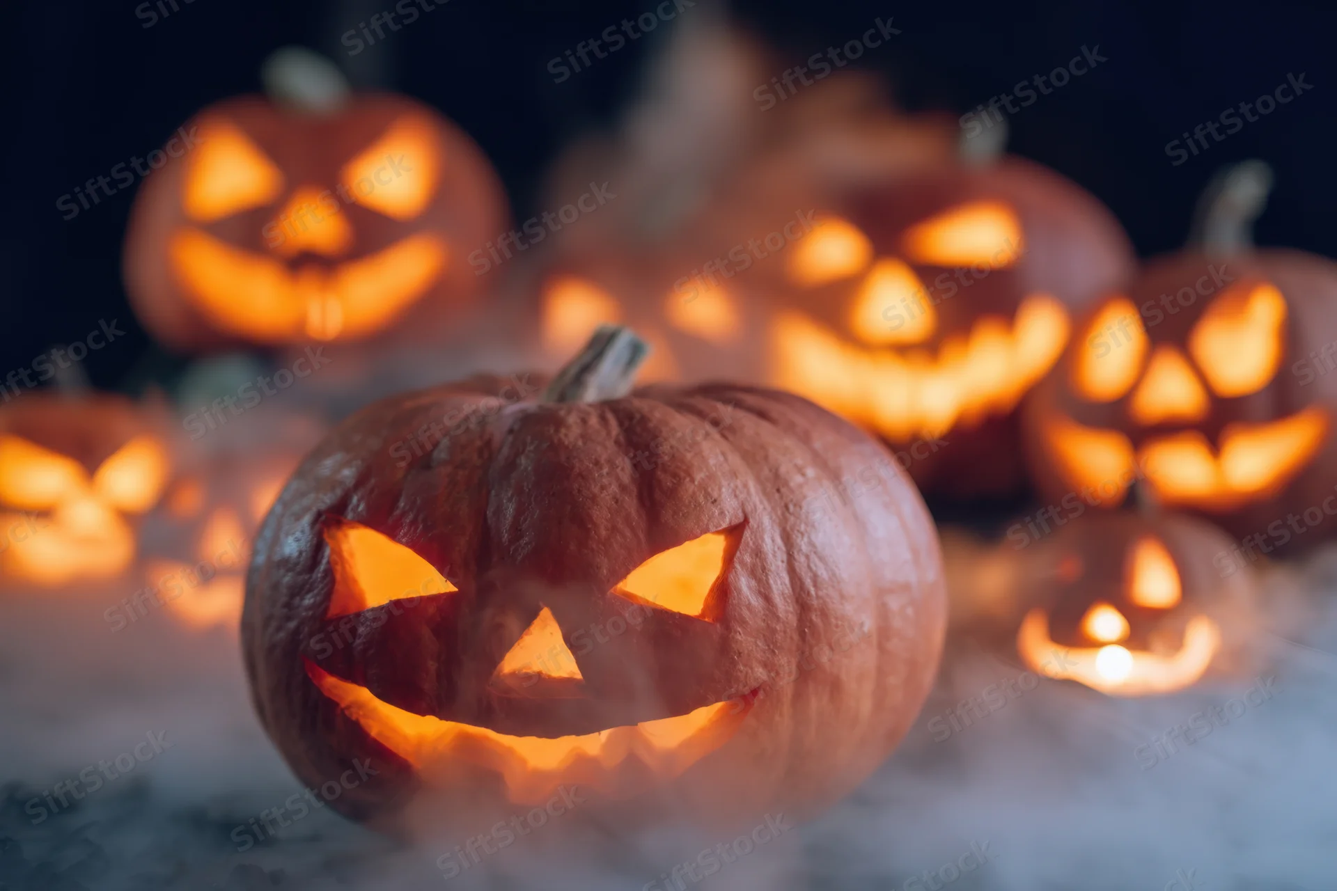 Glowing carved pumpkins arranged on a smoky surface at night for halloween decoration
