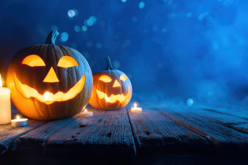 Two carved pumpkins glowing with candles on a wooden table at night