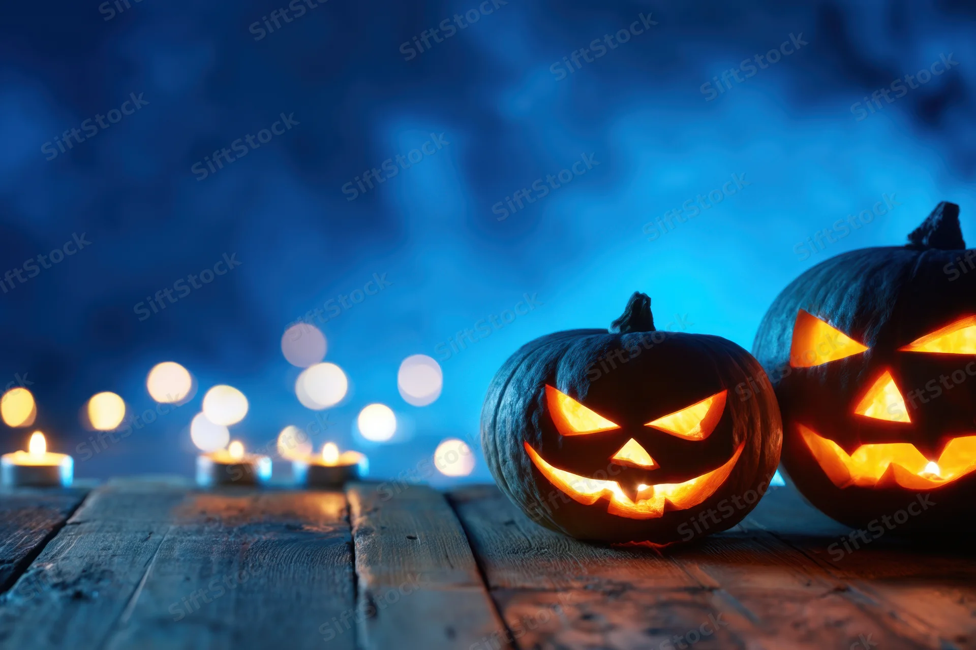 Two carved pumpkins glowing with candles on a wooden table at night