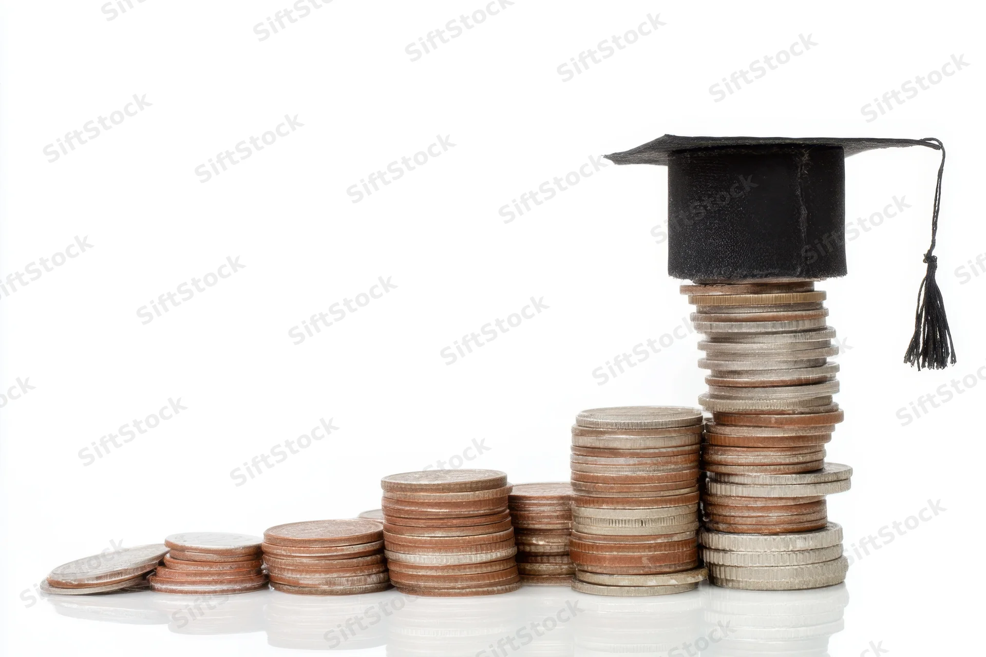 Stacks of coins arranged in ascending order topped with a graduation cap on a white surface