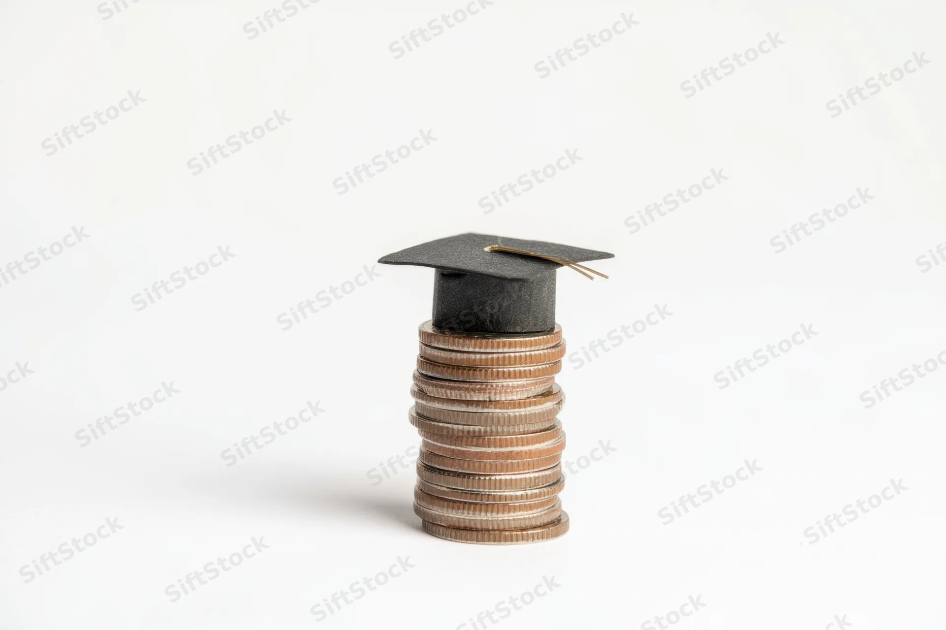 Stack of coins topped with a small graduation cap on white background