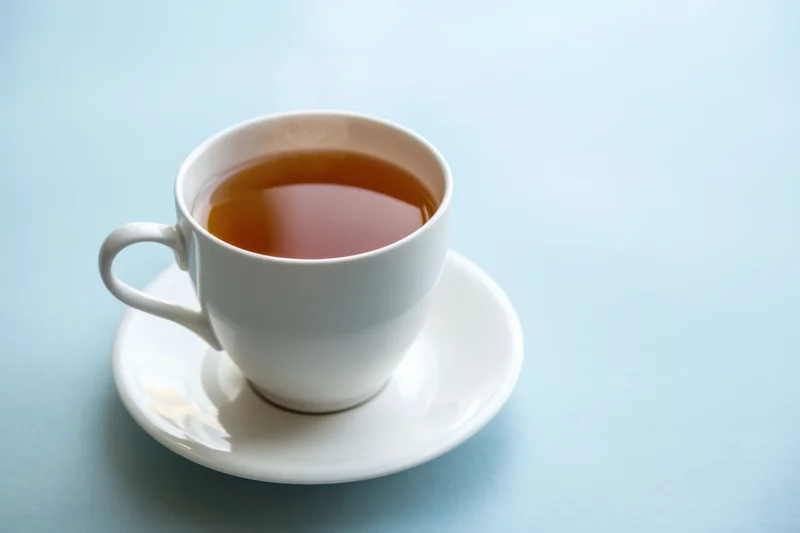 Steaming cup of tea on a white saucer against a light blue background