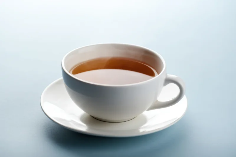 Steaming cup of tea on a white saucer against a light blue surface