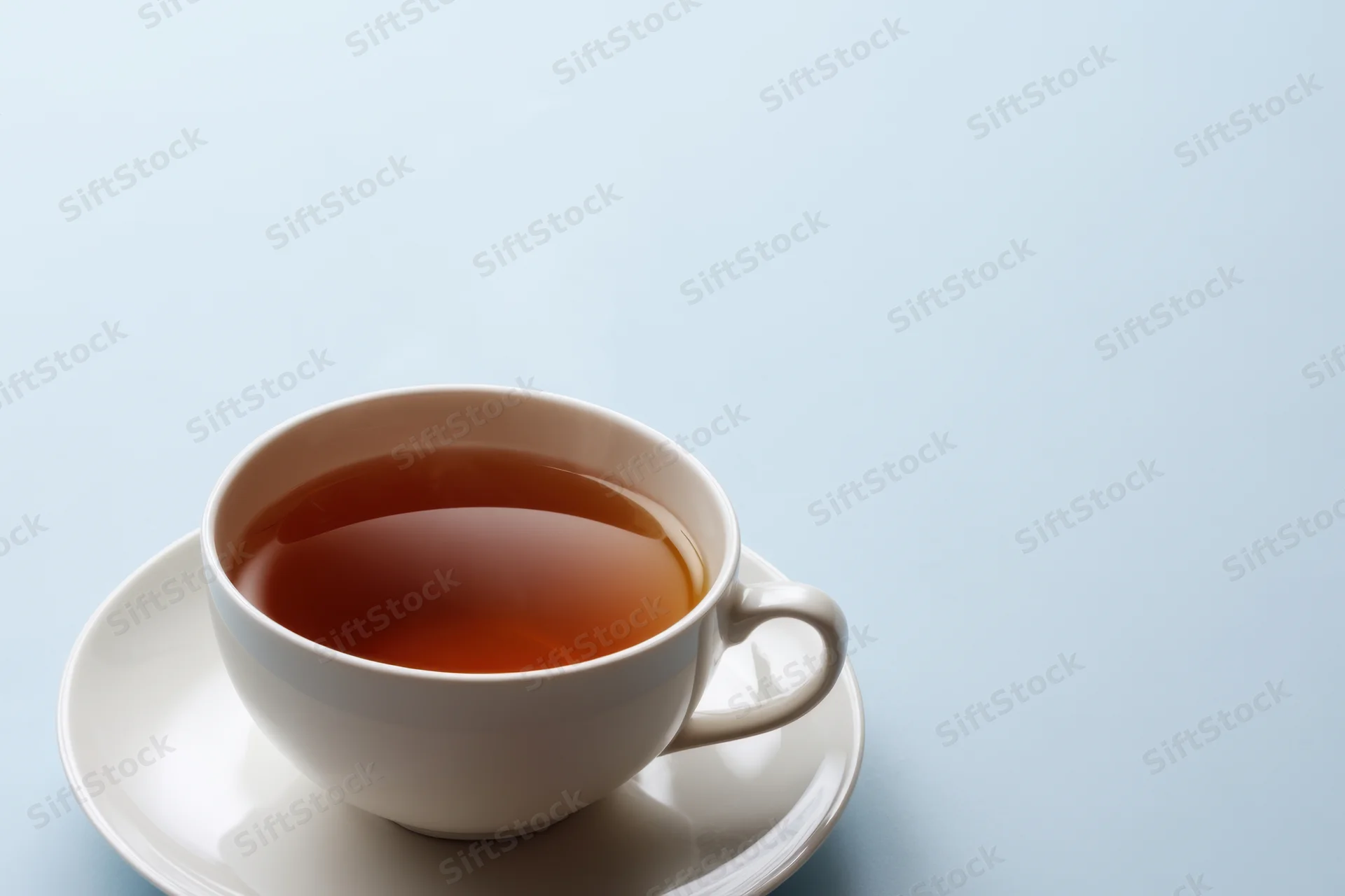Steaming cup of tea on a white saucer against a light blue background