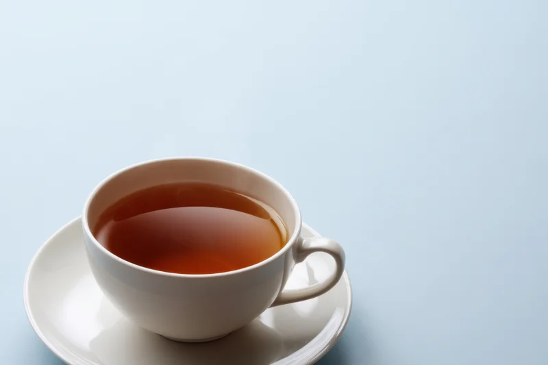 Steaming cup of tea on a white saucer against a light blue background
