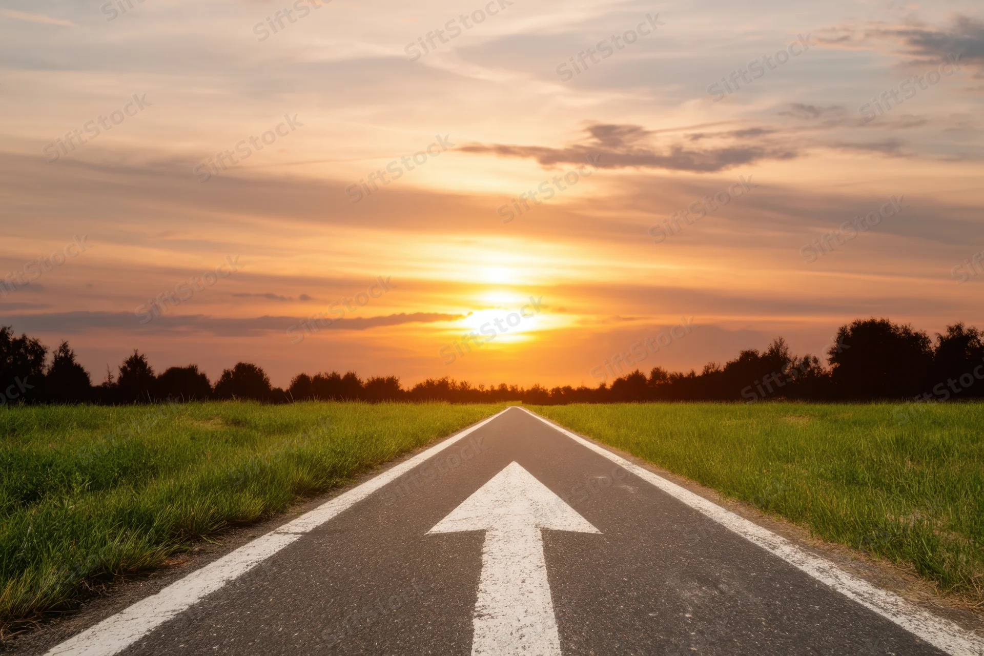 Straight asphalt road with white arrow marking leading toward sunset over grassy field