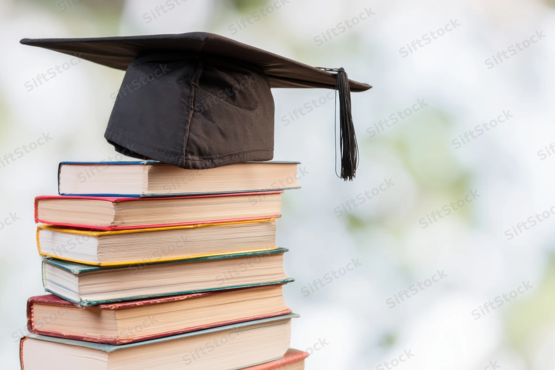 Stack of colorful books topped with a graduation cap against a blurred background