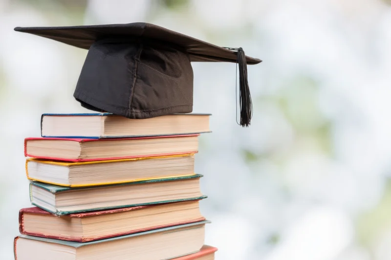 Stack of colorful books topped with a graduation cap against a blurred background