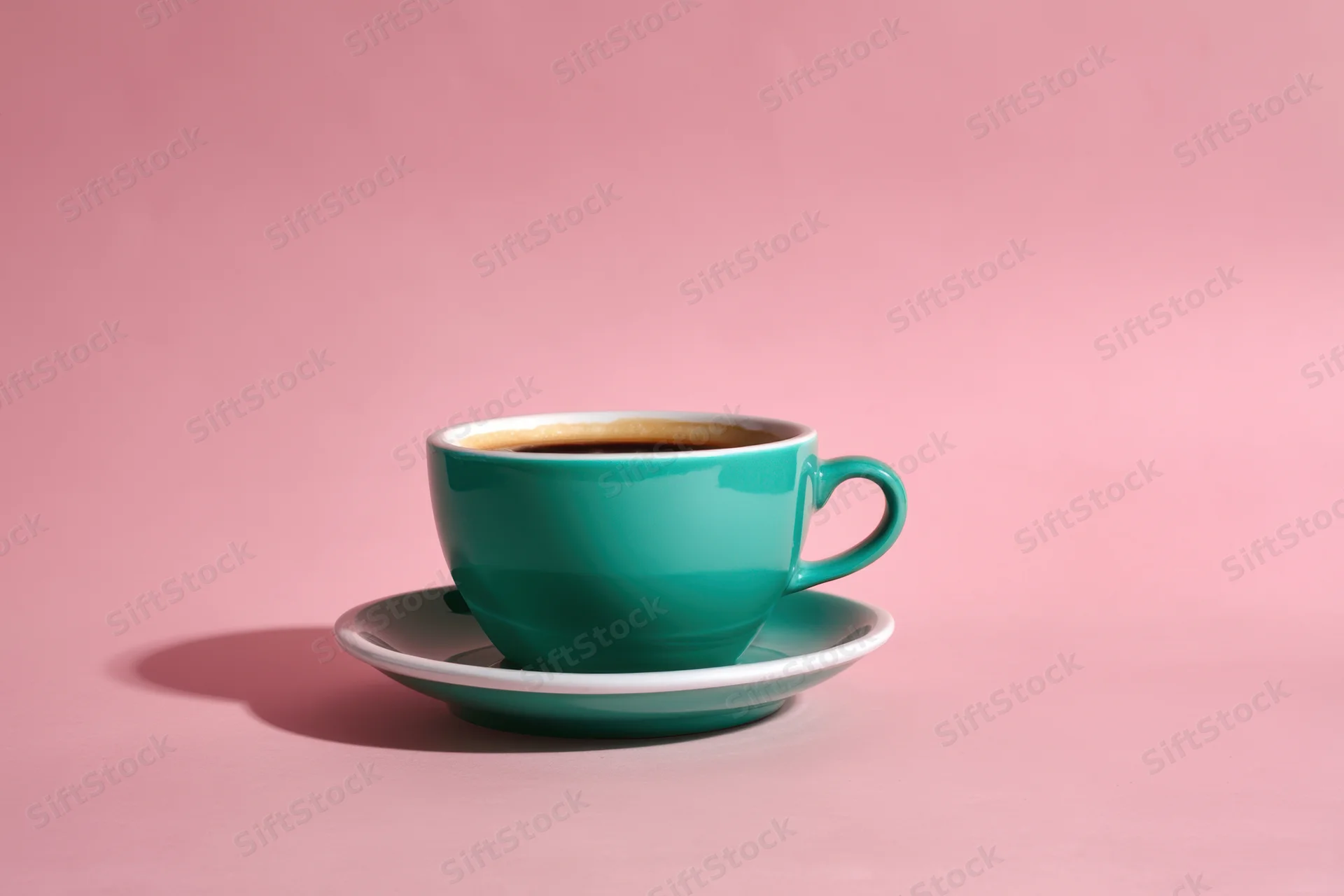 Teal coffee cup on matching saucer against pink background