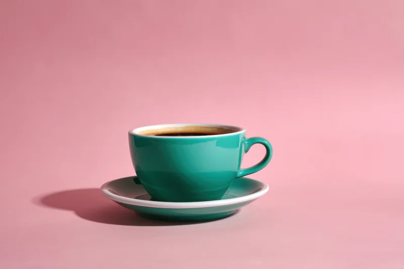 Teal coffee cup on matching saucer against pink background