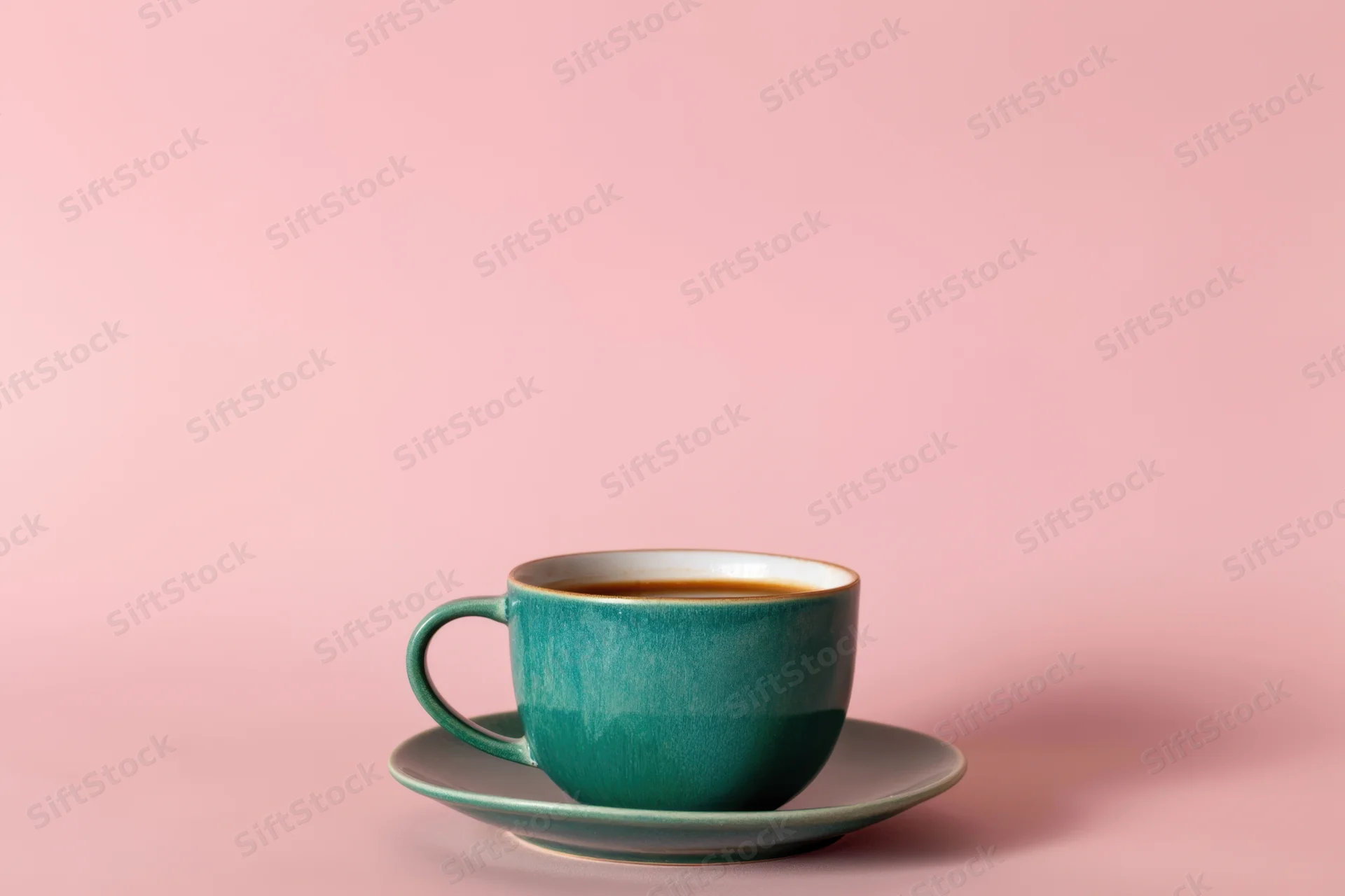 Teal ceramic coffee cup on matching saucer against pink background