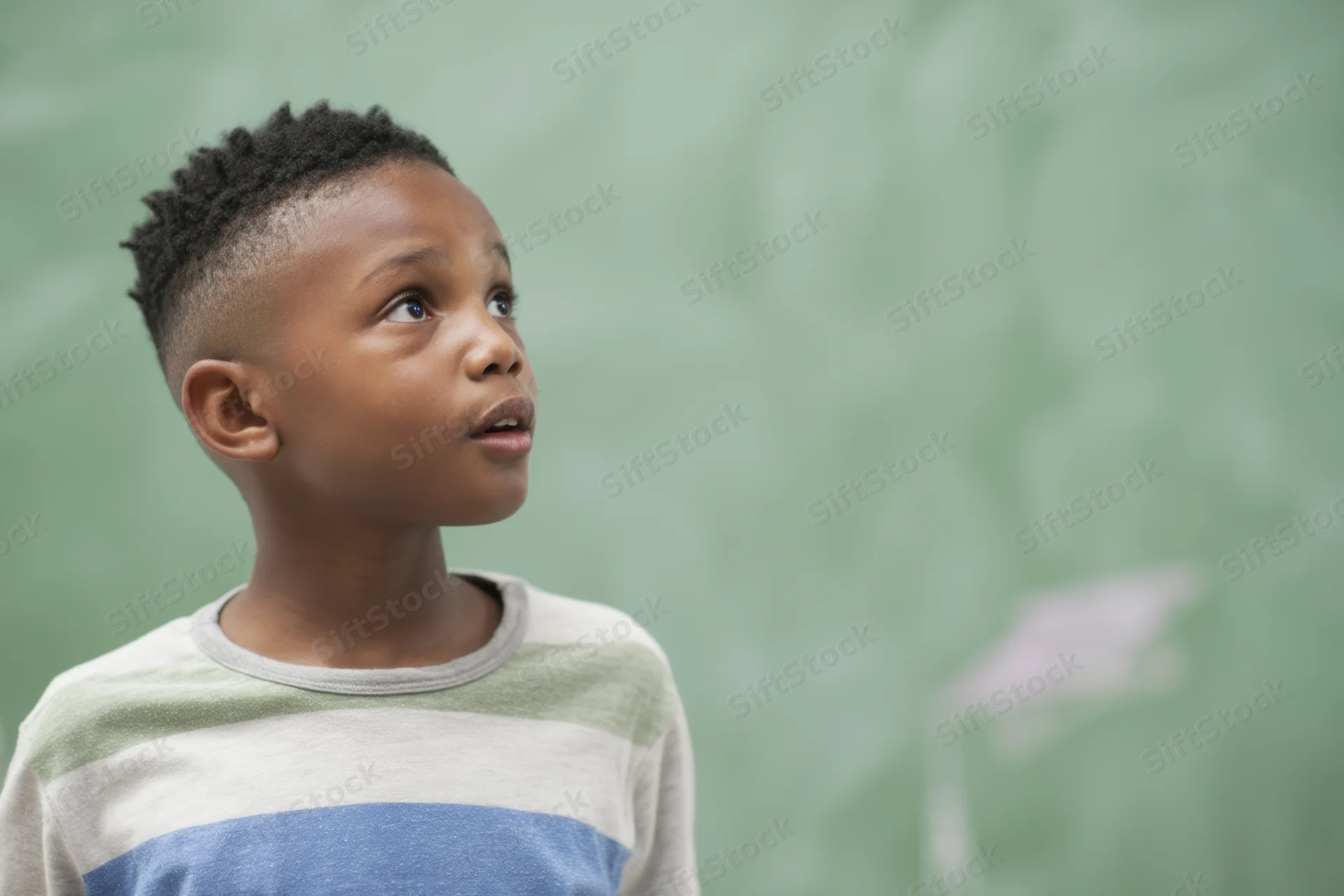 Young black boy looking up thoughtfully in a classroom near a green chalkboard