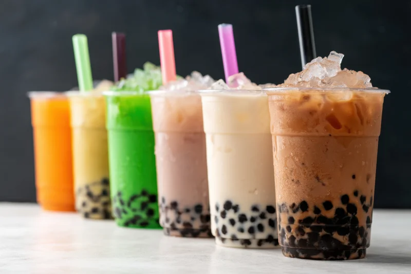 Lineup of colorful bubble tea drinks with tapioca pearls and straws on a light surface