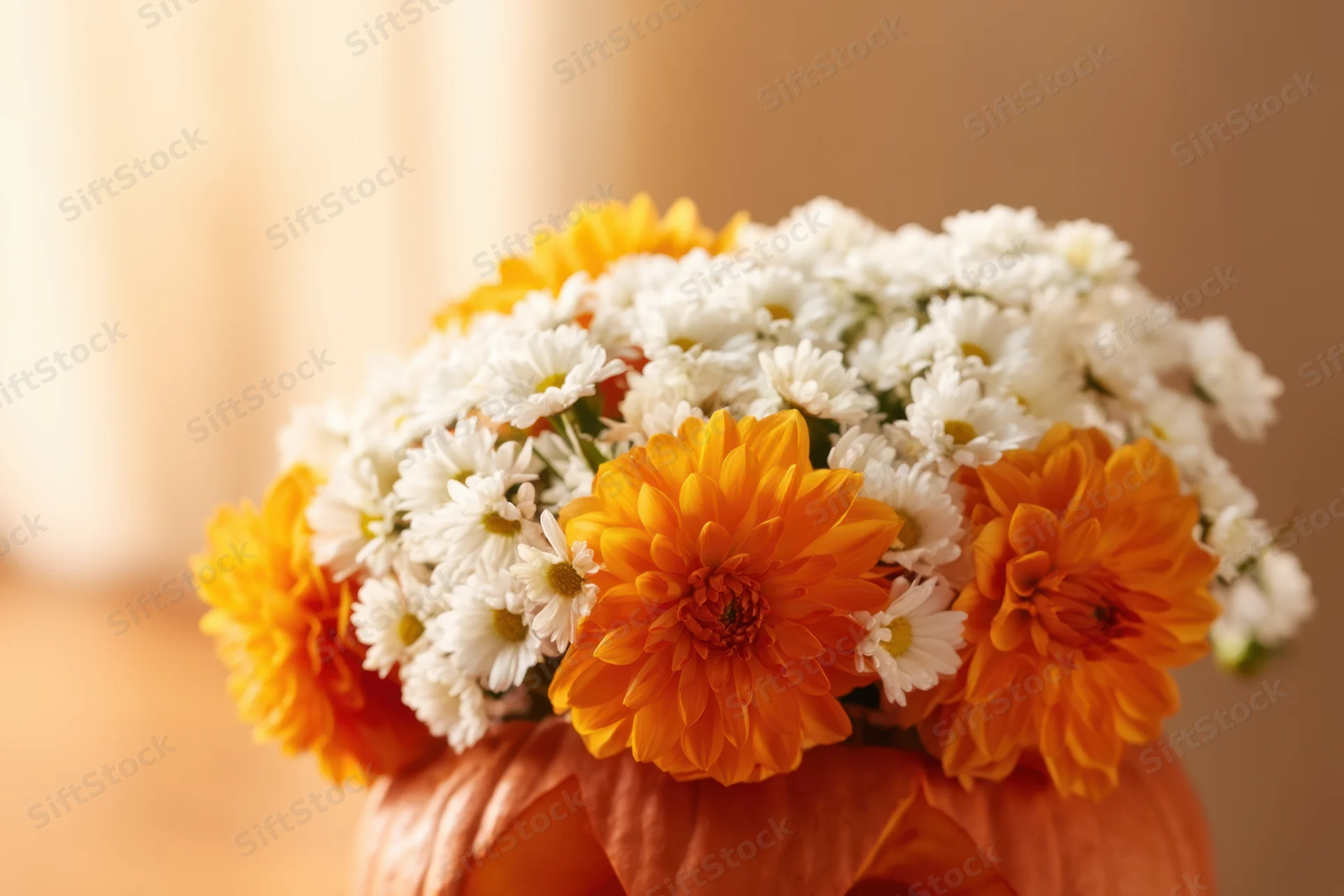 Floral arrangement of orange chrysanthemums and white daisies nestled in a carved pumpkin for halloween decoration
