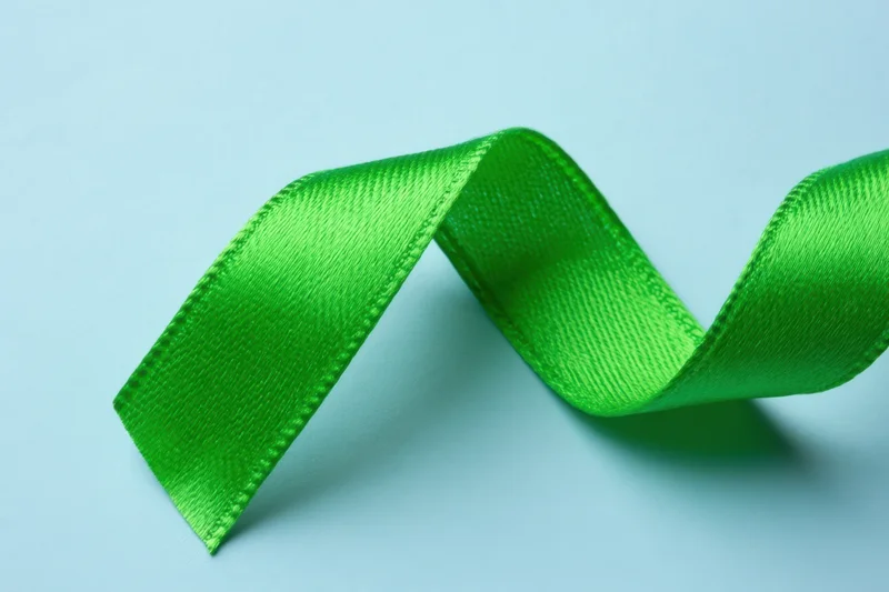 Vibrant green awareness ribbon arranged in a flowing curve on a soft light blue surface