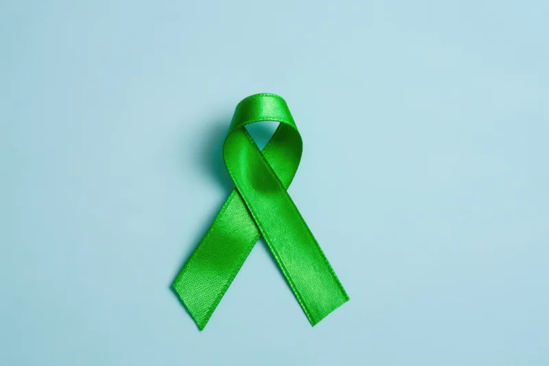 Green awareness ribbon arranged in loop on light blue surface