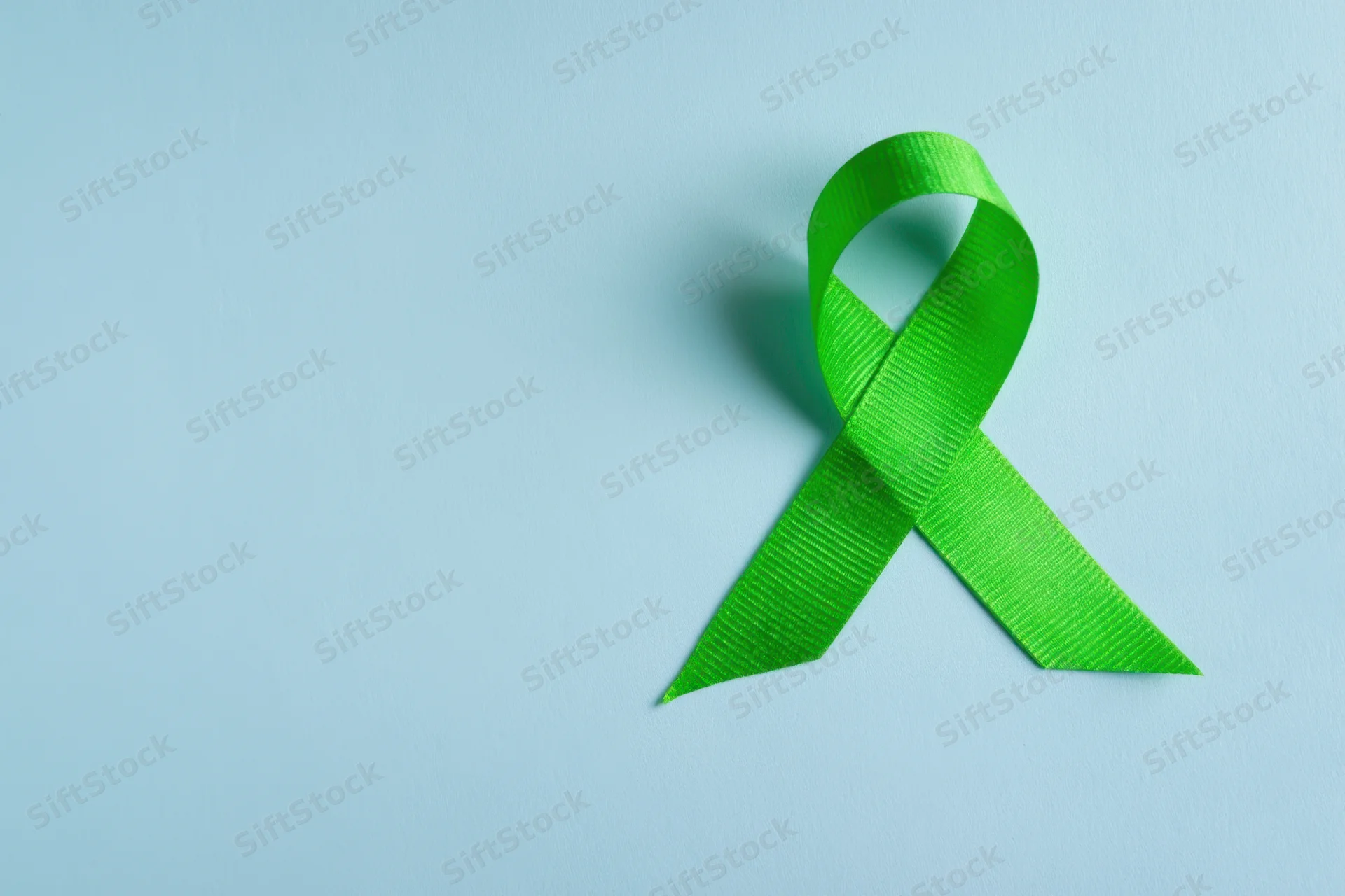 Green awareness ribbon arranged in loop on soft blue background