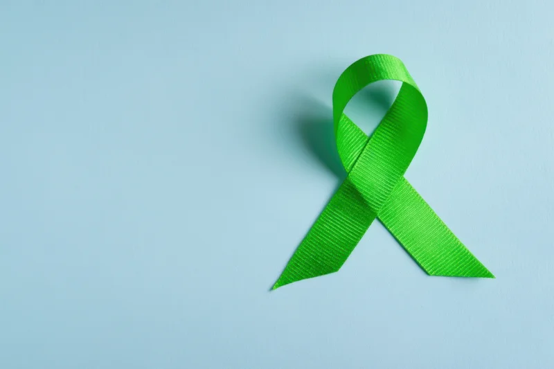 Green awareness ribbon arranged in loop on soft blue background