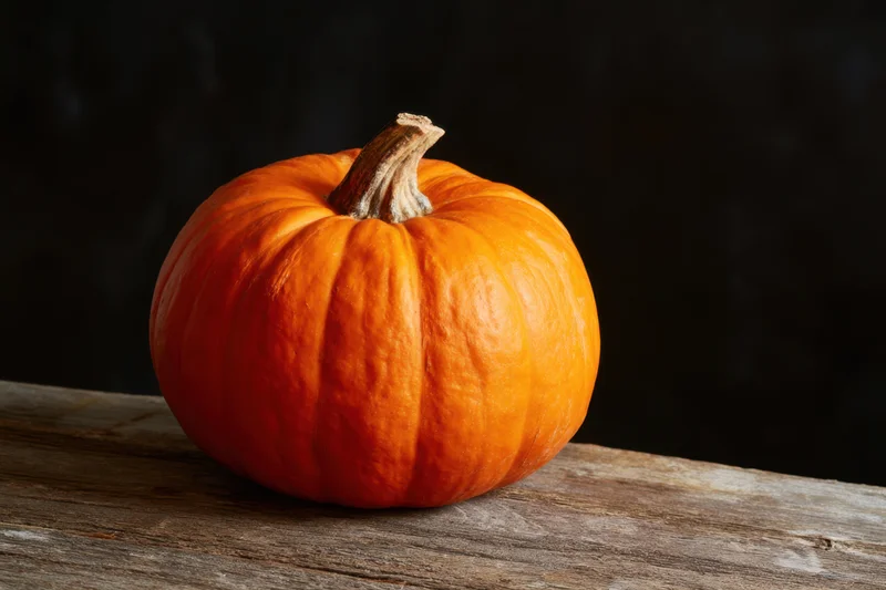 Orange pumpkin resting on weathered wooden surface against dark background