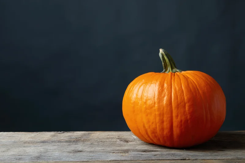 Orange pumpkin resting on weathered wooden surface against dark background