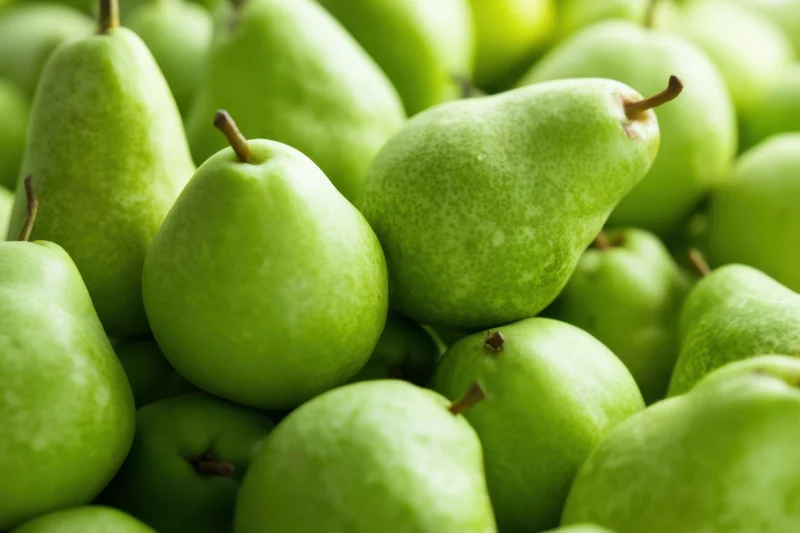 A pile of fresh green pears arranged closely together showcasing their smooth skin and natural texture