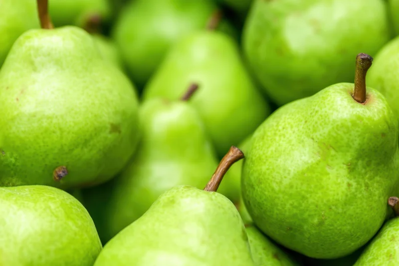 A pile of fresh green pears arranged closely together showcasing their smooth skin and stems