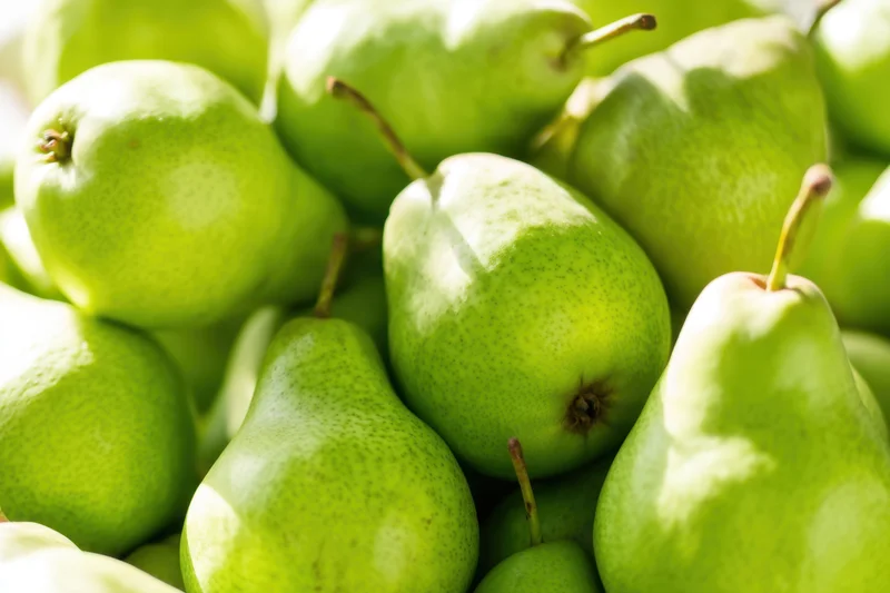 A pile of fresh green pears arranged closely together, showcasing their smooth skin and stems