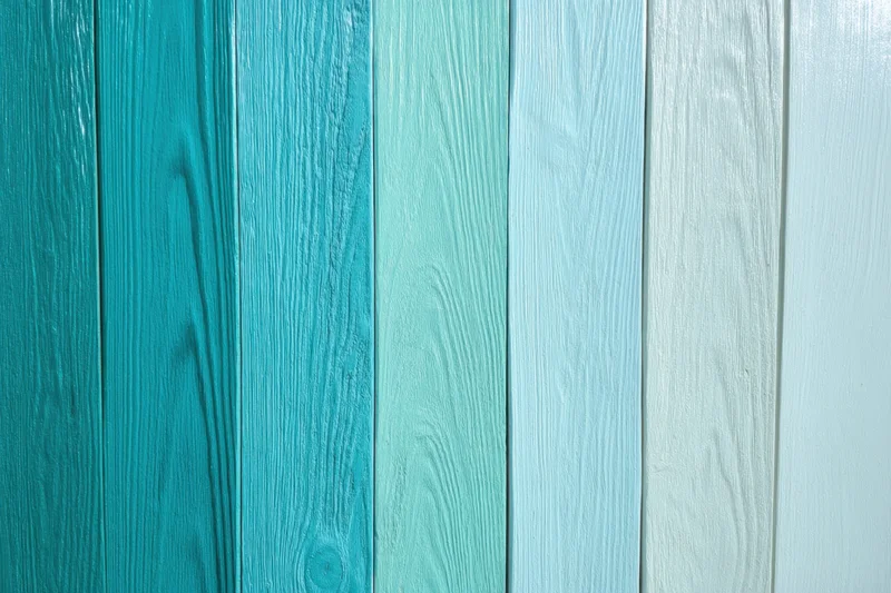 Vertical wooden panels arranged in a gradient from deep teal to white forming a wall surface