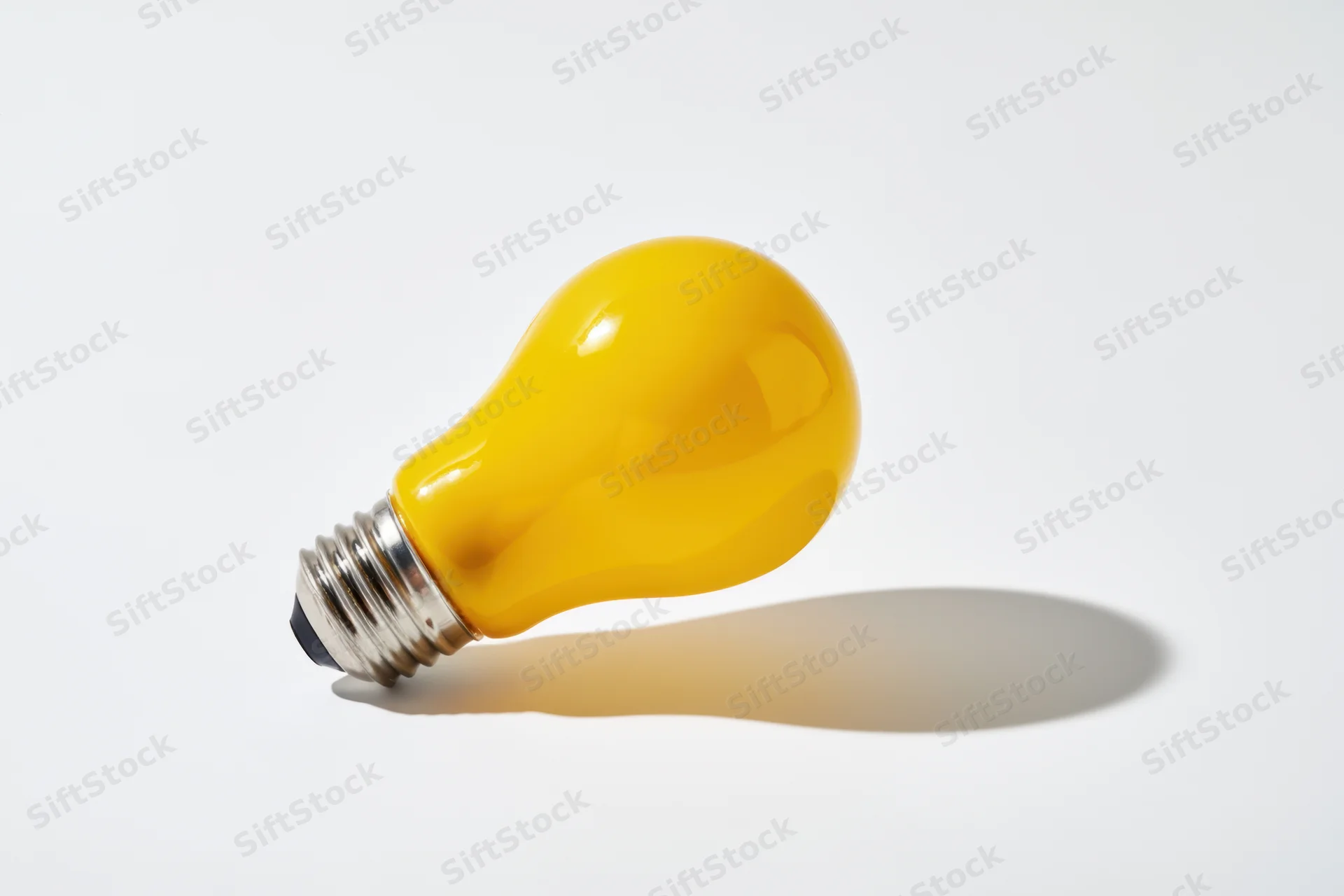 Yellow lightbulb lying on white surface casting soft shadow