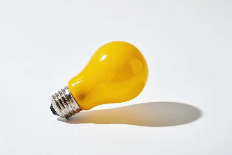 Yellow lightbulb lying on white surface casting soft shadow