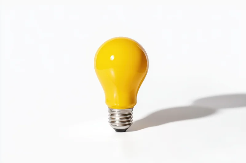 Yellow lightbulb standing upright on white surface casting shadow