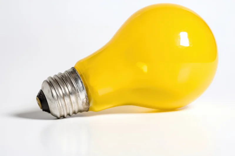Yellow lightbulb lying on white surface with screw base visible