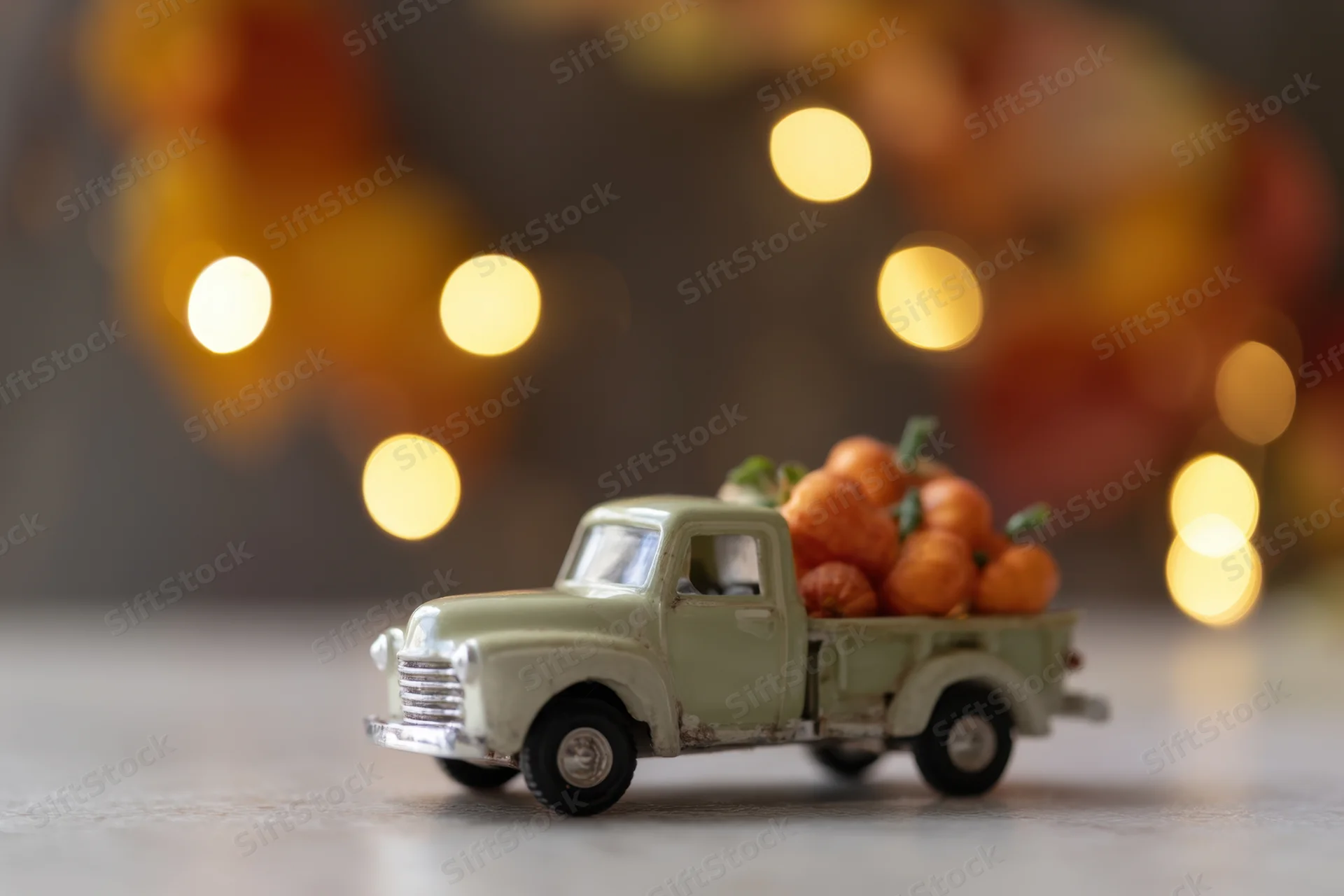Vintage toy truck carrying small decorative pumpkins on a table with warm bokeh lights in the background