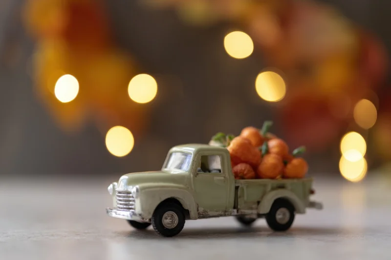 Vintage toy truck carrying small decorative pumpkins on a table with warm bokeh lights in the background