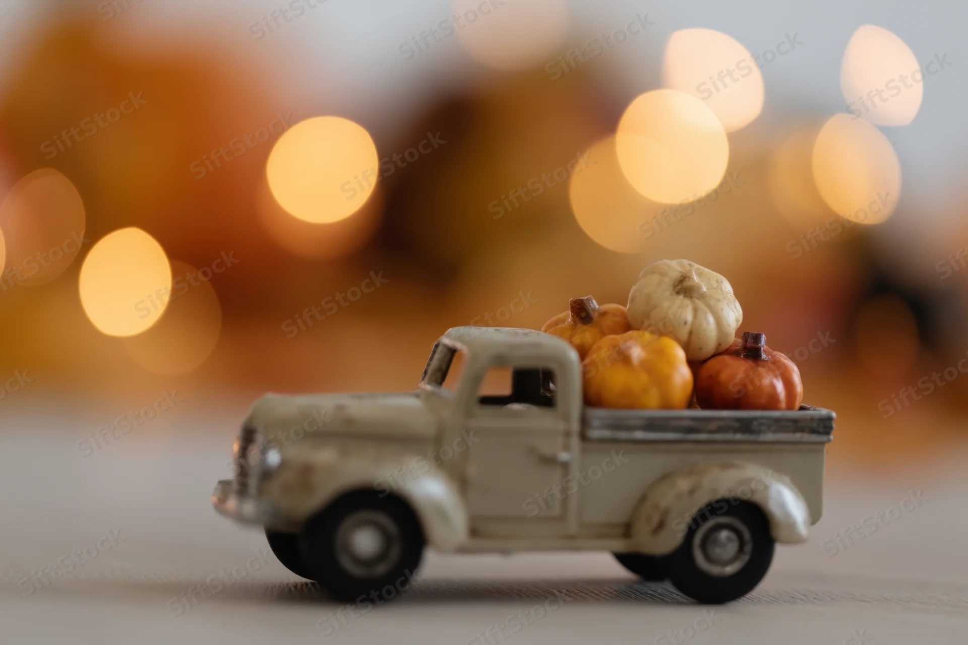 Vintage toy truck carrying small decorative pumpkins on a tabletop with warm bokeh background